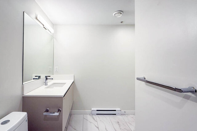 bathroom with white countertop vanity, large mirror, marble tile flooring, grab bar, and partial view of toilet