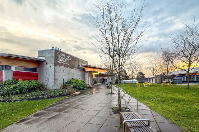 The building exterior shows the Trout Lake Community Centre with a paved walkway, green lawn, bicycle racks, and yellow outdo