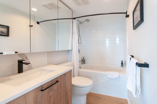 Modern bathroom with white tile, curved shower, and wooden vanity. - 3006 - 33 Smithe Street, Vancouver Downtown