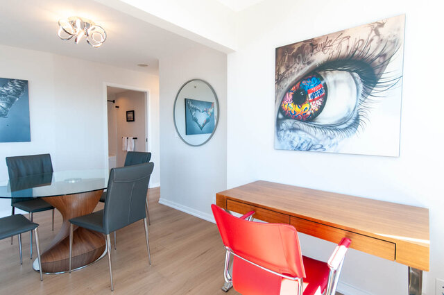 Modern dining area with a glass table, vibrant red chairs, and a large eye artwork on the wall. - 3006 - 33 Smithe Street, Vancouver Downtown