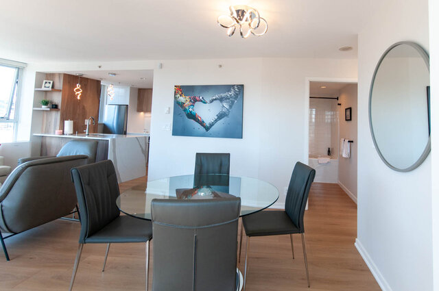 Modern dining area with glass table, gray chairs, and vibrant heart artwork on the wall. - 3006 - 33 Smithe Street, Vancouver Downtown