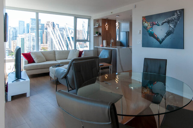 Modern open-concept living room with hardwood floors, a cozy sectional sofa, and a stunning city view through large windows.
