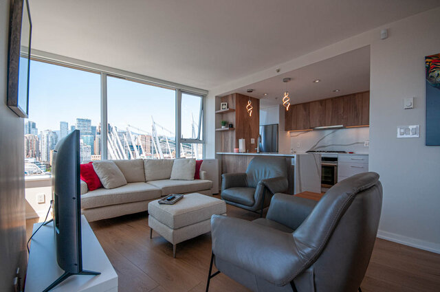 Open-concept living space with hardwood floors, a cozy sectional sofa, and a city view from large windows.