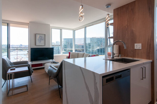 Modern kitchen with sleek white countertops and hardwood floors, featuring a city view. - 3006 - 33 Smithe Street, Vancouver Downtown