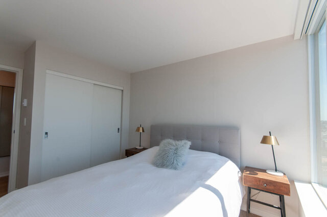 Spacious bedroom with a large window offering a city view, modern furniture, and a cozy bed setup. - 3006 - 33 Smithe Street, Vancouver Downtown