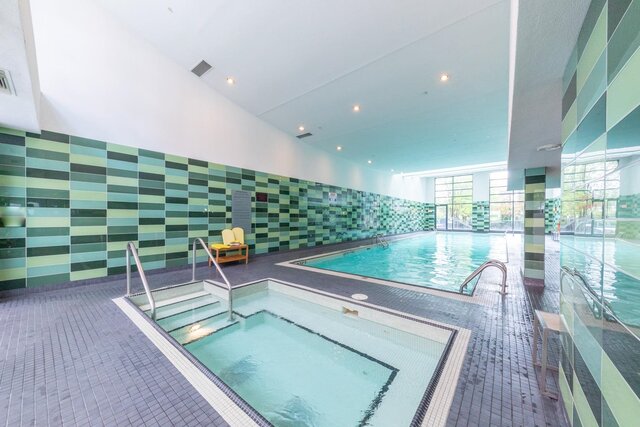 Spacious, modern 1-bedroom + den condo with a bright, well-lit indoor pool area featuring green mosaic tiles and a hot tub.