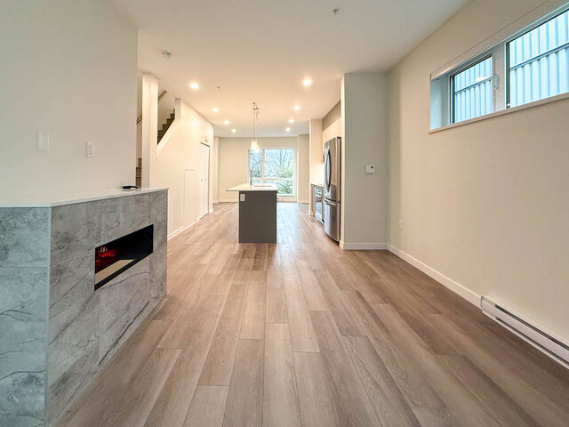 Open-concept living room with hardwood floors, modern fireplace, and kitchen island. - TH 13 - 2030 East 20th Ave, Vancouver East Side