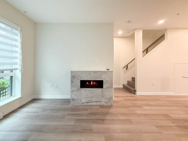 Open living room with modern fireplace, hardwood floors, and a view of the staircase. - TH 13 - 2030 East 20th Ave, Vancouver East Side