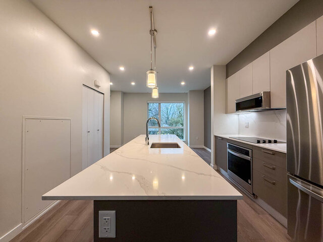 Modern kitchen with white marble countertops and stainless steel appliances, featuring a large island and a city view.
