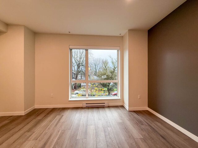 Spacious living room with hardwood floors and a large window showcasing a city view. - TH 13 - 2030 East 20th Ave, Vancouver East Side