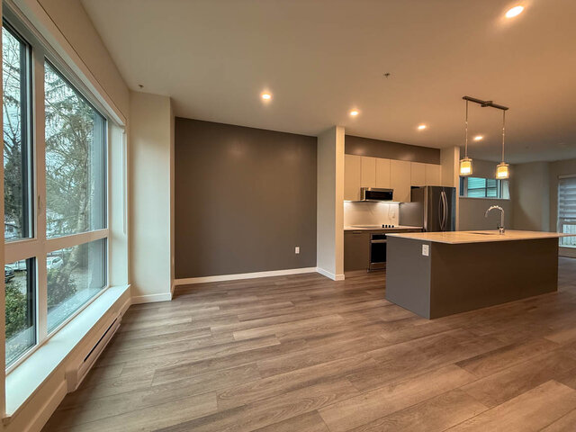 Open-concept living space with hardwood floors, modern kitchen island, and large windows offering a city view.