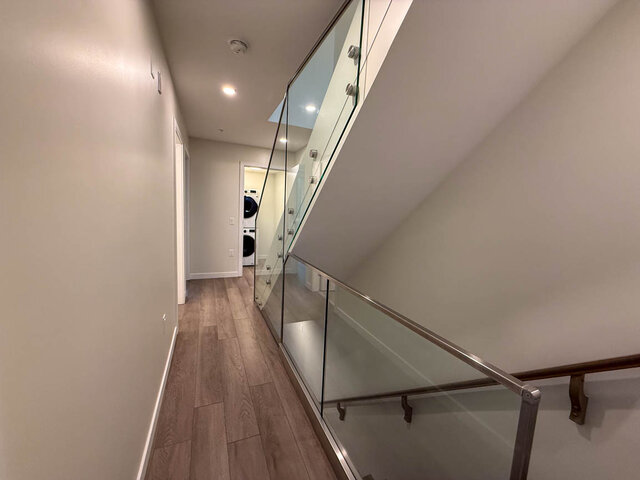 Modern hallway with glass railing and hardwood floors leading to a laundry area. - TH 13 - 2030 East 20th Ave, Vancouver East Side