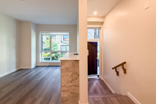 Bright kitchen with marble countertop and hardwood floors, leading to a cozy living area with a city view.