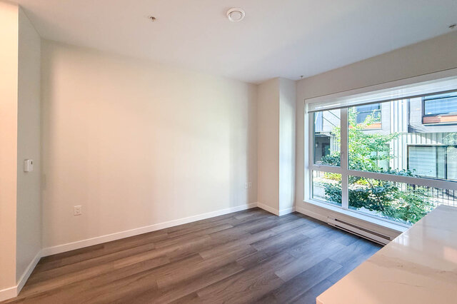 Spacious living room with hardwood floors and large windows offering a view of greenery. - TH 46- 2050 East 20th Ave, Vancouver East Side