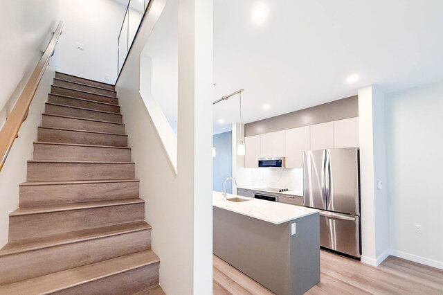 Modern kitchen with white countertops and stainless steel appliances, adjacent to a staircase with wooden steps.