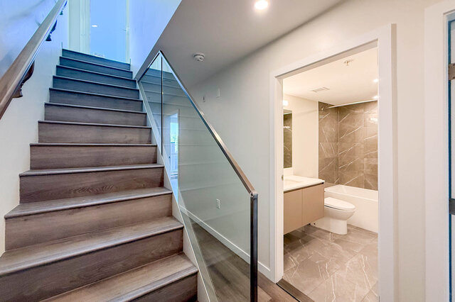 Modern bathroom with beige tiles and a sleek sink, adjacent to a stylish staircase with glass railings.