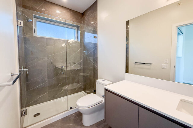 Modern bathroom with a walk-in shower, large mirror, and sleek countertop. - TH 46- 2050 East 20th Ave, Vancouver East Side