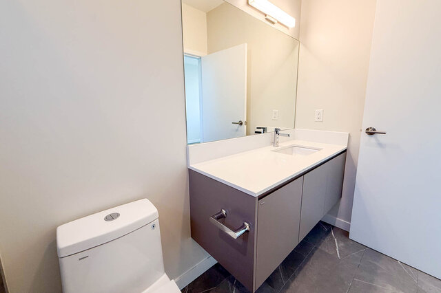 Modern bathroom with sleek white countertop and large mirror, featuring a contemporary design. - TH 46- 2050 East 20th Ave, Vancouver East Side