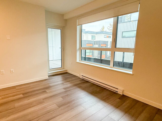 Empty living area with a large window and a glass door out to the balcony - 302-3588 Hull St, Vancouver East Side