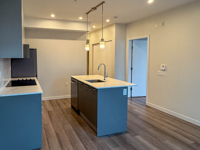 Kitchen island with a dishwasher and pendant lights, looking toward an open doorway - 302-3588 Hull St, Vancouver East Side