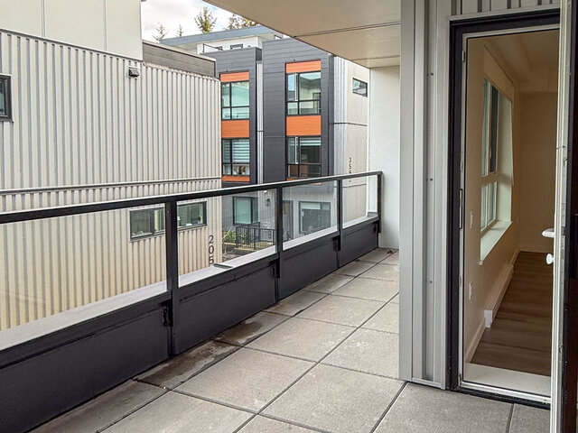 Private balcony with a glass railing and pavers, looking across at neighbouring townhomes - 302-3588 Hull St, Vancouver East Side