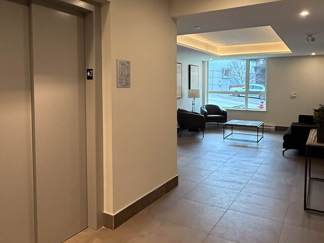 Building lobby with lounge chairs by a big window, next to the elevator - 302-3588 Hull St, Vancouver East Side