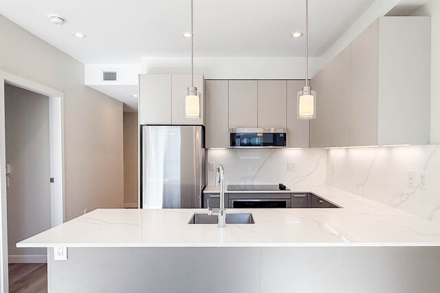 Bright kitchen with white island countertops and modern stainless steel appliances on hardwood floors. - 400 - 3588 Hull St, Vancouver East Side