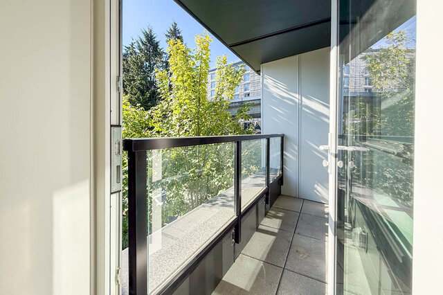 Open-plan living area with light wood hardwood floors and modern kitchen island. - 400 - 3588 Hull St, Vancouver East Side