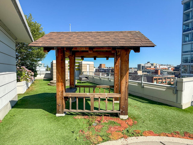 This balcony features a wooden gazebo structure, a city view in the background, and landscaped plants on one side.