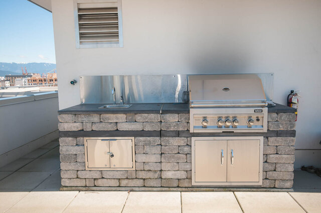The balcony has an outdoor kitchen with stainless steel grill, sink, stone countertop, and fire extinguisher.