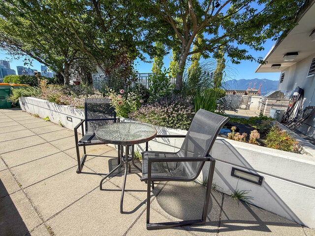 The balcony features outdoor seating with a small table and chairs, surrounded by landscaping and offering city and mountain 
