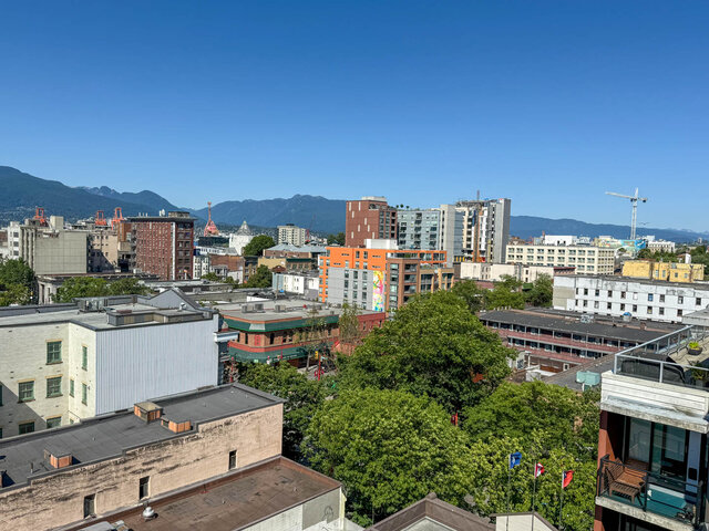 Building exterior showing city buildings, greenery, mountains in the background, clear blue sky, and construction cranes.
