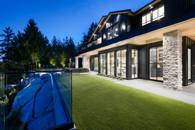 Spacious living room with glass railings, modern furnishings, and a view of the night sky. - 4589 Woodgreen Drive, West Vancouver