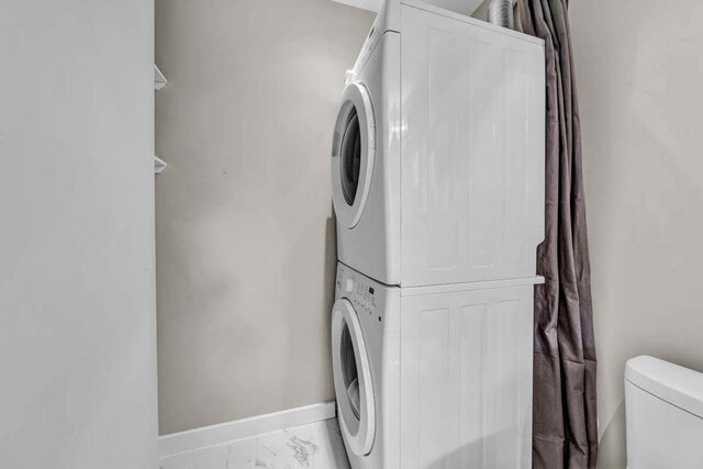 Spacious laundry room with white stacked washer and dryer, marble countertop, and neutral walls. - 4393 West 3rd Ave, Vancouver West Side