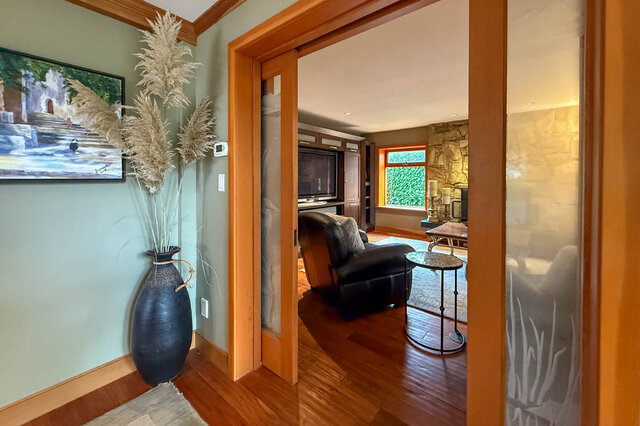 Spacious living room with hardwood floors, a cozy recliner, and a stone accent wall. - 3850 Point Grey Road, Vancouver West Side