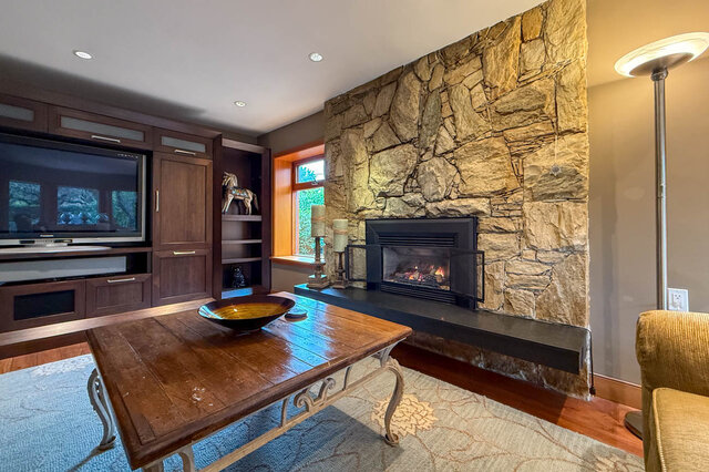 Cozy living room with stone fireplace, hardwood floors, and a large TV setup. - 3850 Point Grey Road, Vancouver West Side