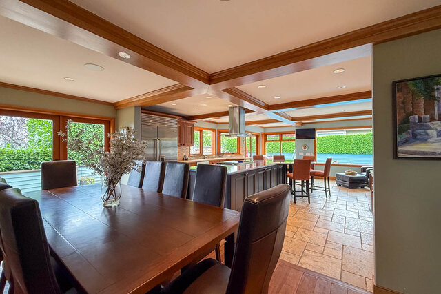 Open-concept kitchen and dining area with hardwood floors, modern appliances, and a view of greenery outside.