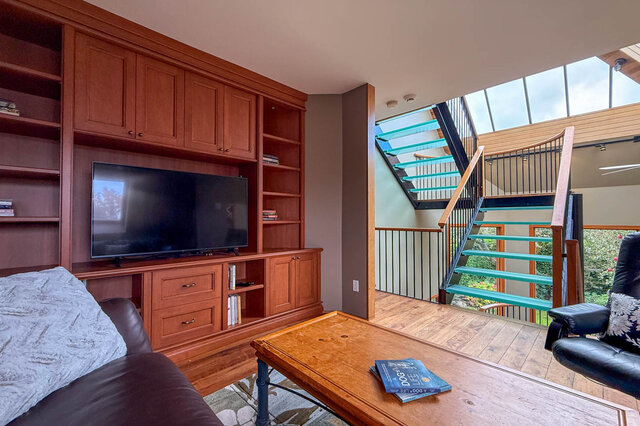 Spacious living room with built-in entertainment center, modern staircase, and natural light from skylight.