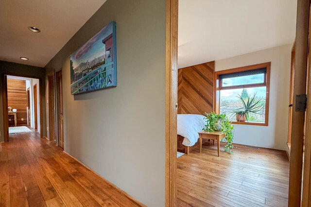 Spacious bedroom with hardwood floors and a cityscape painting, featuring a cozy bed and a window with a scenic view.