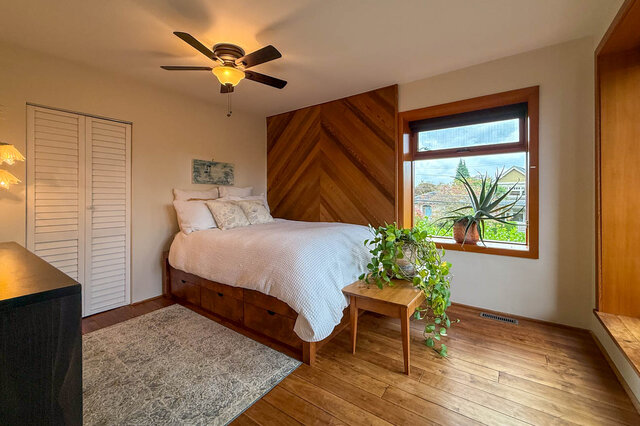 Cozy bedroom with wooden accent wall, hardwood floors, and a city view through the window. - 3850 Point Grey Road, Vancouver West Side