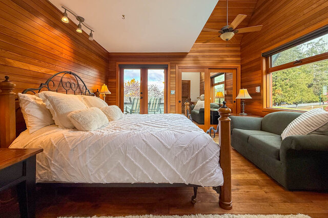 Spacious master bedroom with wooden walls, large windows, and a cozy bed setup. - 3850 Point Grey Road, Vancouver West Side
