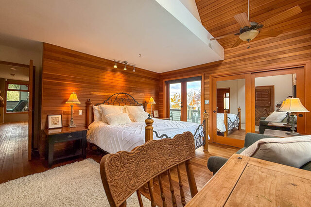 Spacious master bedroom with wooden walls, king-sized bed, and large sliding glass doors leading to a balcony.