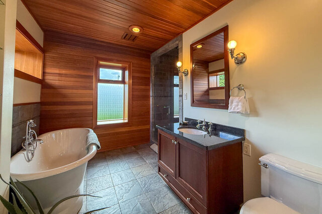 Spacious bathroom with wooden paneling, black countertops, and a freestanding tub. - 3850 Point Grey Road, Vancouver West Side