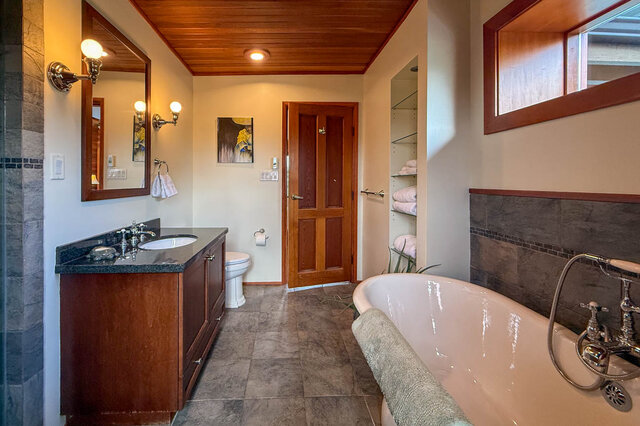 Spacious bathroom with dark stone countertops and wooden accents, featuring a large soaking tub and a walk-in closet.