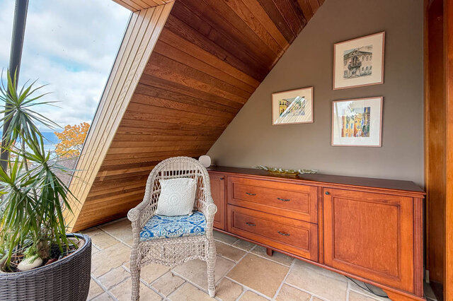 Cozy attic bedroom with wooden paneling, a wicker chair, and framed cityscape art. - 3850 Point Grey Road, Vancouver West Side