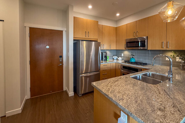 Modern kitchen with granite countertops, stainless steel appliances, and light wood cabinets. - 526-119 West 22nd Street, North Vancouver