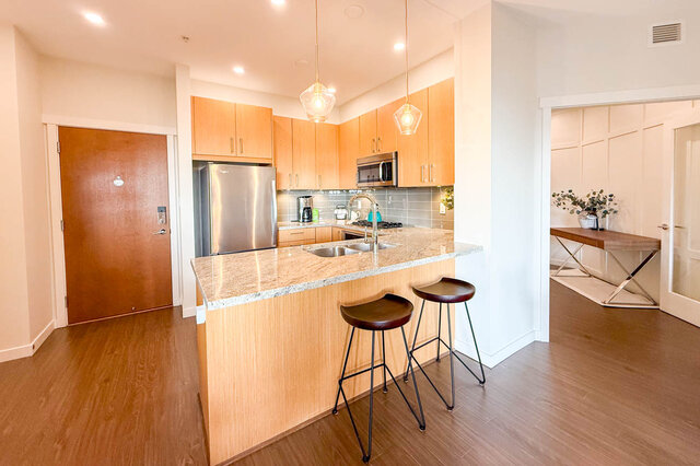 Bright kitchen with granite countertops, wooden cabinets, and modern pendant lights. - 526-119 West 22nd Street, North Vancouver