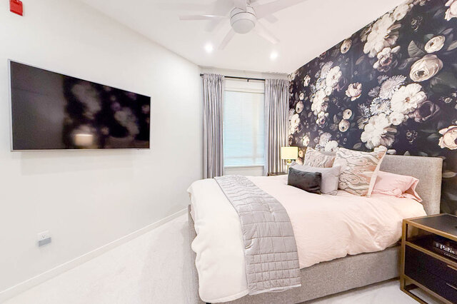 Spacious bedroom with floral accent wall and modern flat-screen TV. - 526-119 West 22nd Street, North Vancouver
