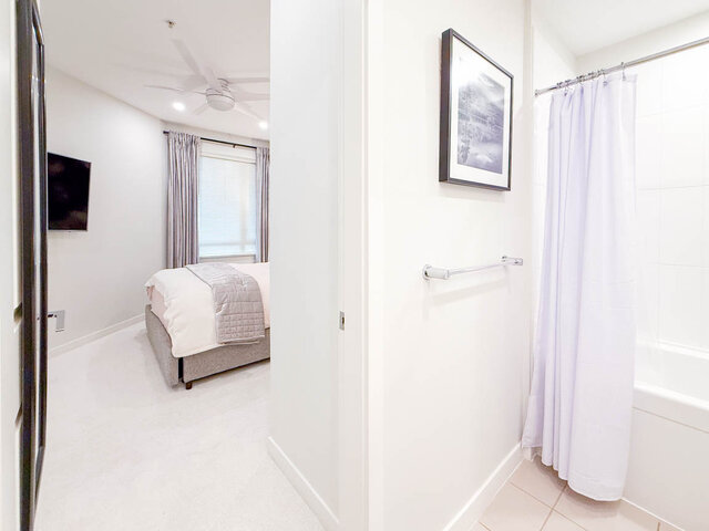 Bright bedroom with cozy bed and flat-screen TV, adjacent to a modern bathroom with shower and towel bar. - 526-119 West 22nd Street, North Vancouver