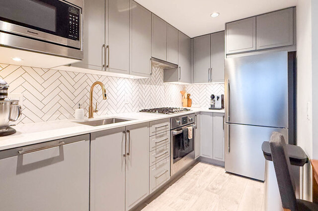 Bright kitchen with white countertops, herringbone backsplash, and stainless steel appliances. - 407-2435 Kingsway, Vancouver East Side